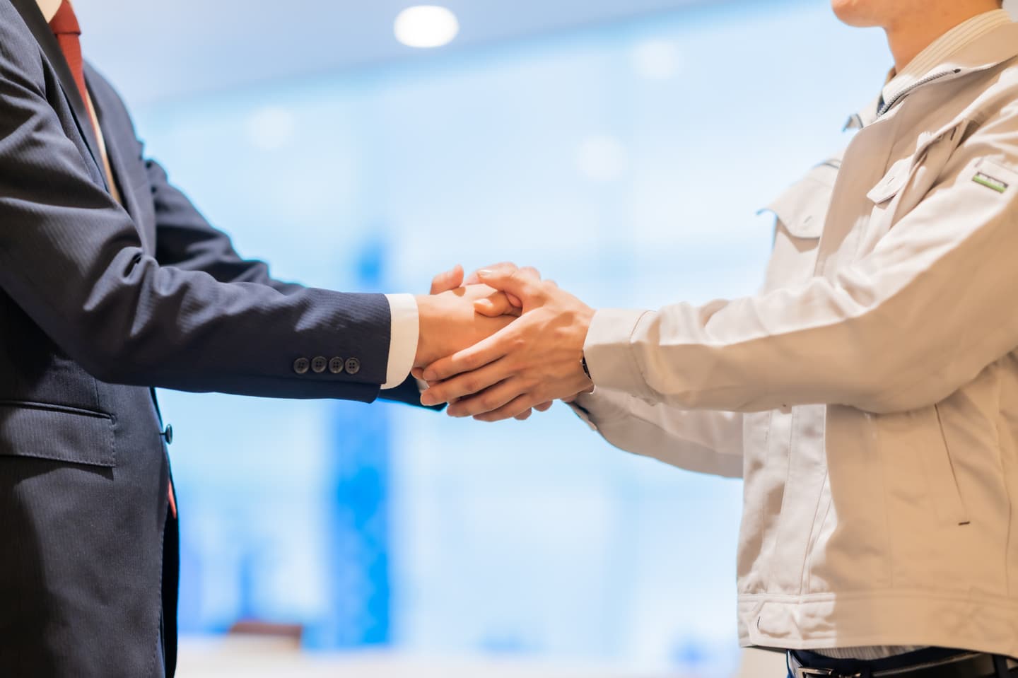 作業着を着た二人が握手を交わしている写真